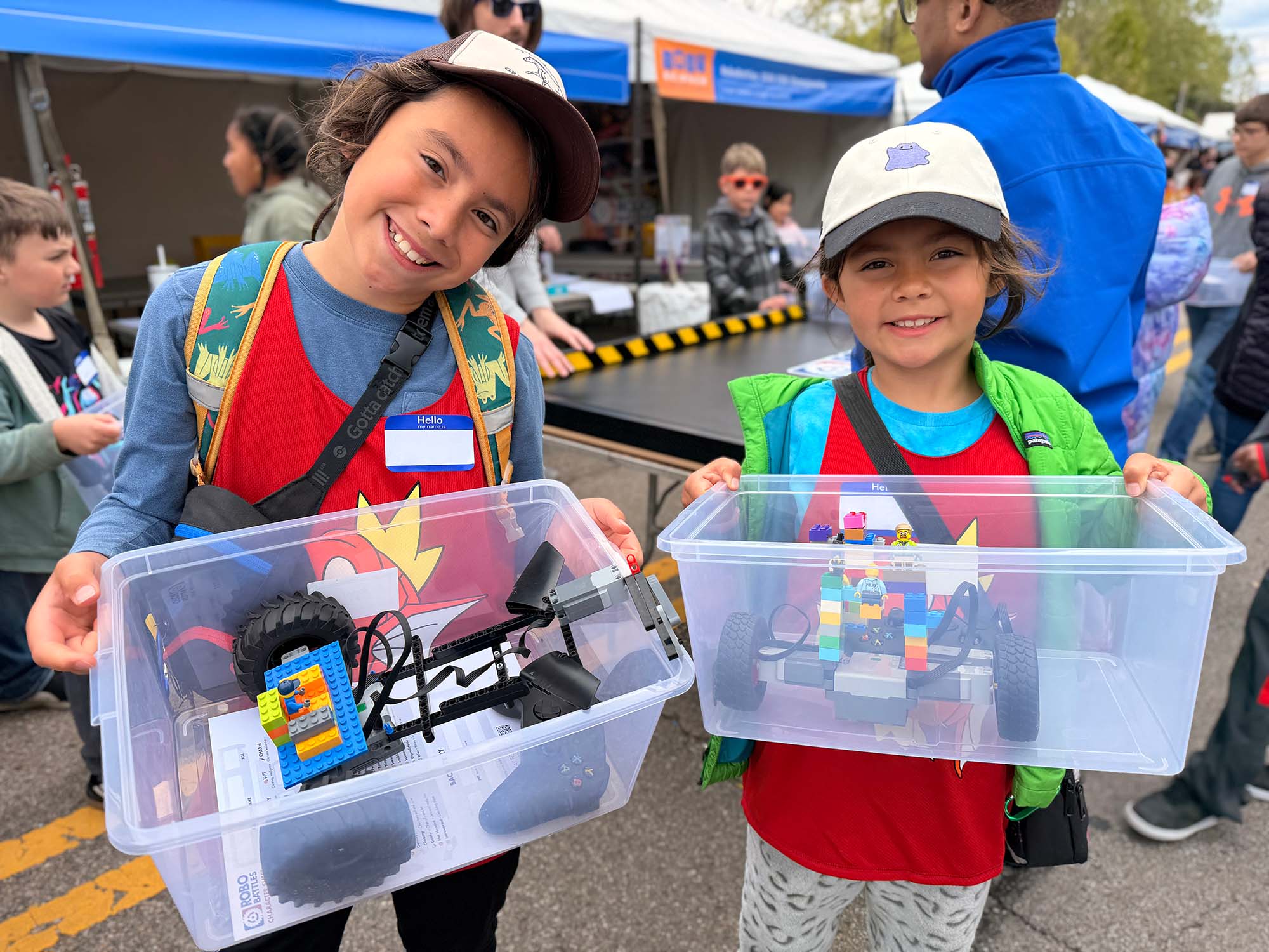 Two players holding bins of LEGO robots and parts