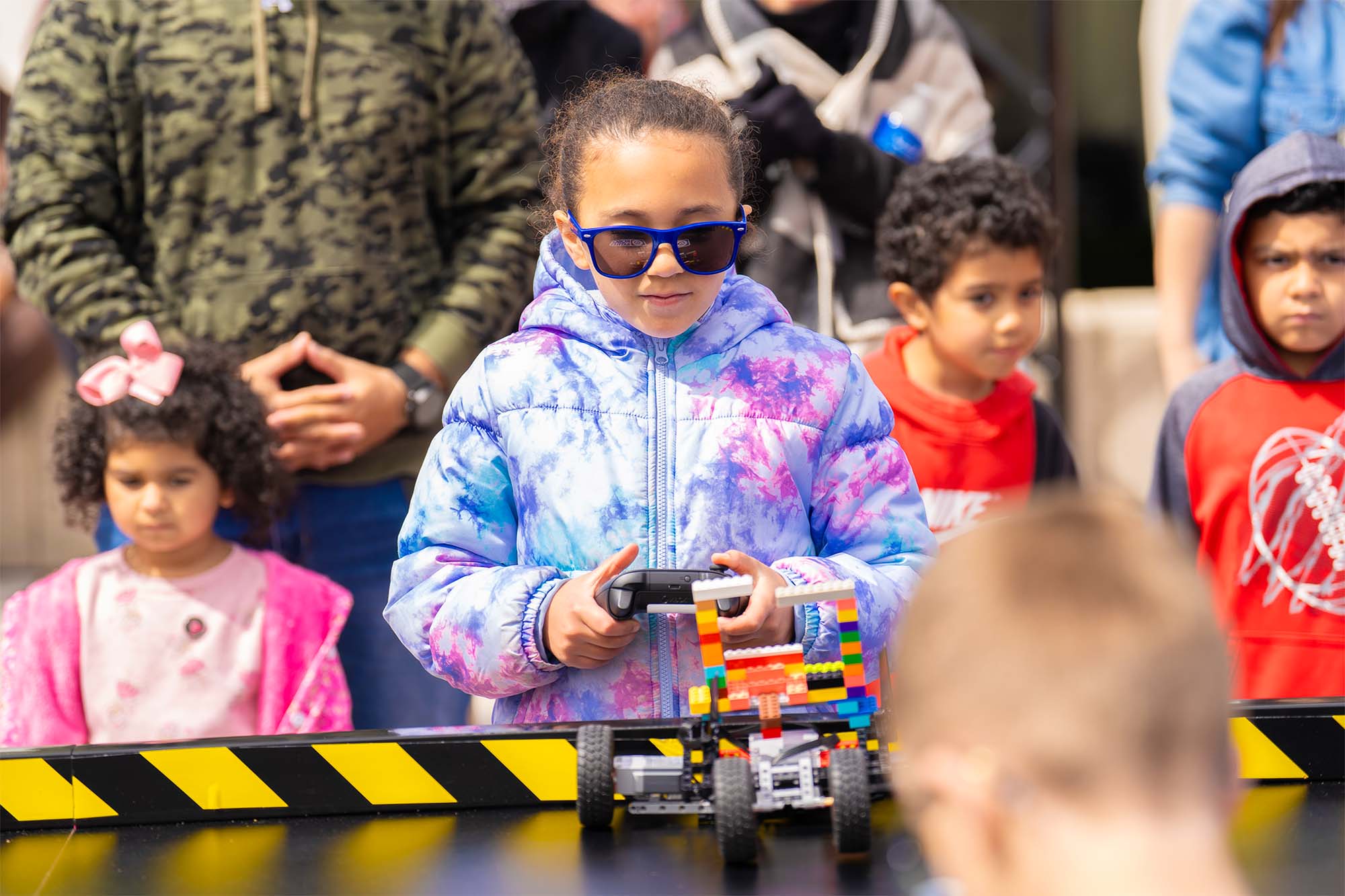 Player in blue sunglasses driving a LEGO robot with a game controller